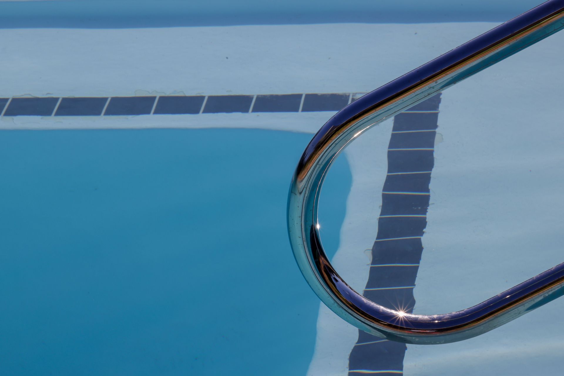 Dynamic view of a swimming pool with ladder reflecting sunlight on the water surface.