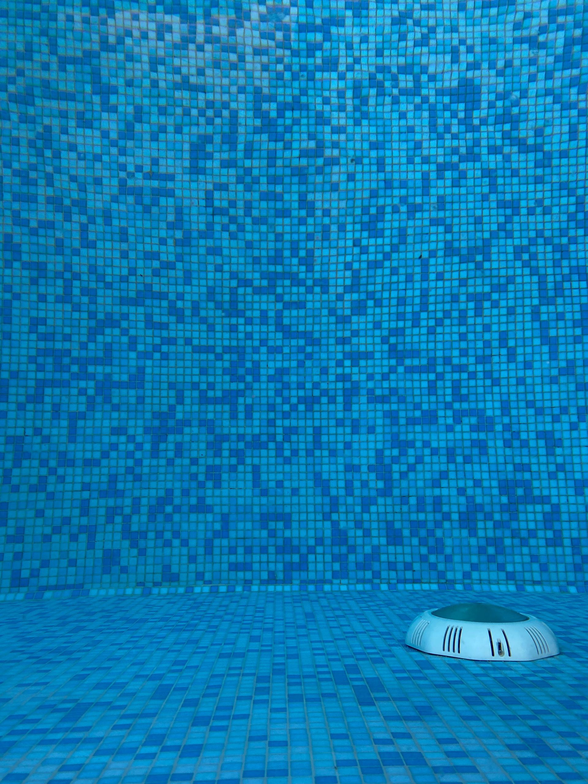 Vibrant blue mosaic tiles in a swimming pool with a visible drain.